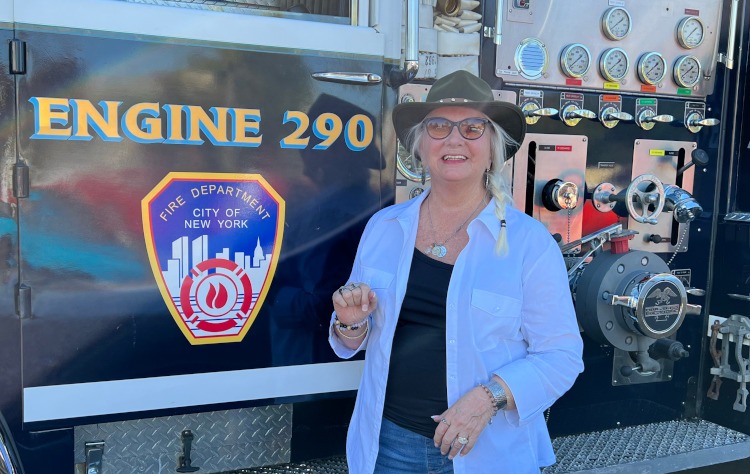 A woman is standing beside a classic blue fire truck.