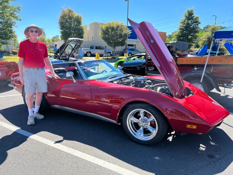 A man standing beside a athird-generation red Corvette.
