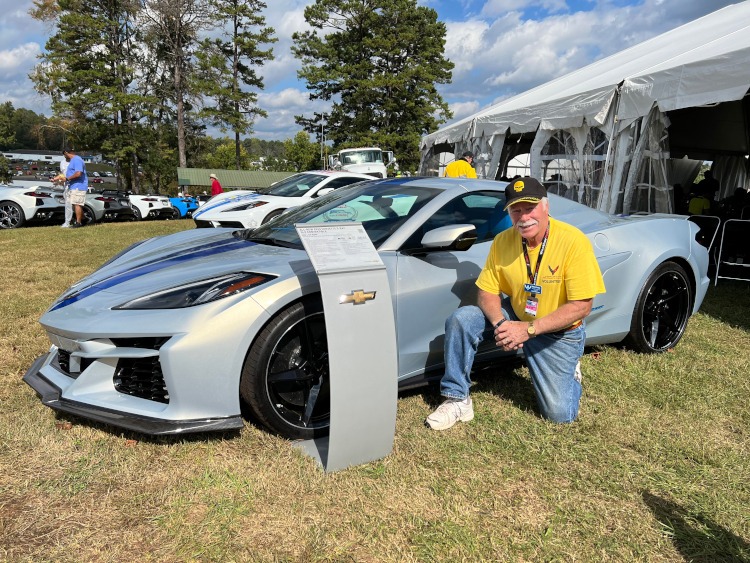 A man is kneeling beside a 2024 Corvette ERay at a race.
