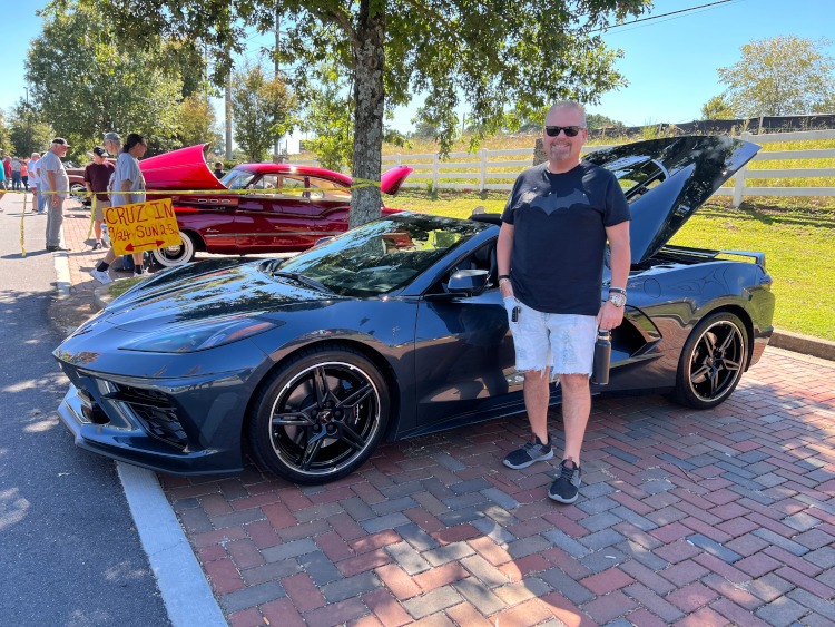 A man is standing beside a black eighth-generation Corvette coupe.