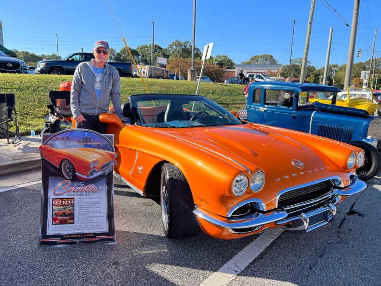 A man is standing beside a custom 1962 Corvette roadster at a car show.