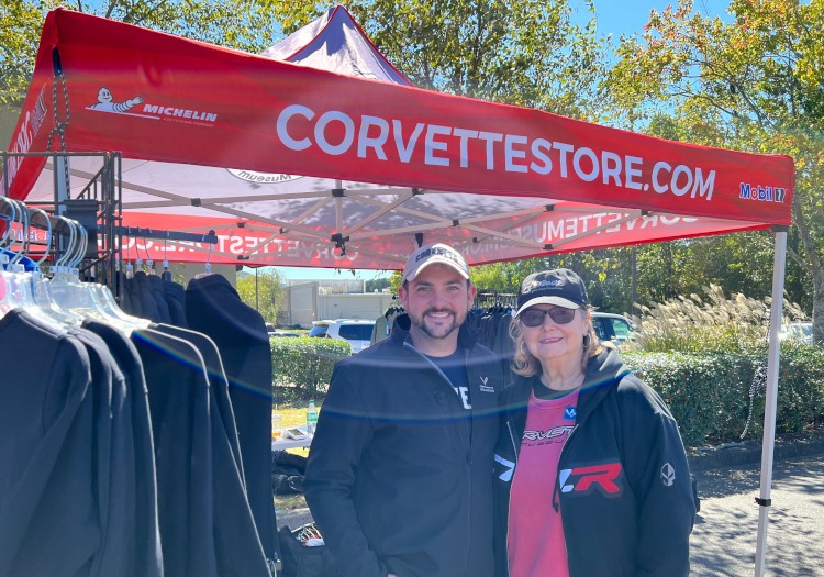 Two people standing under a Corvette Store tent.
