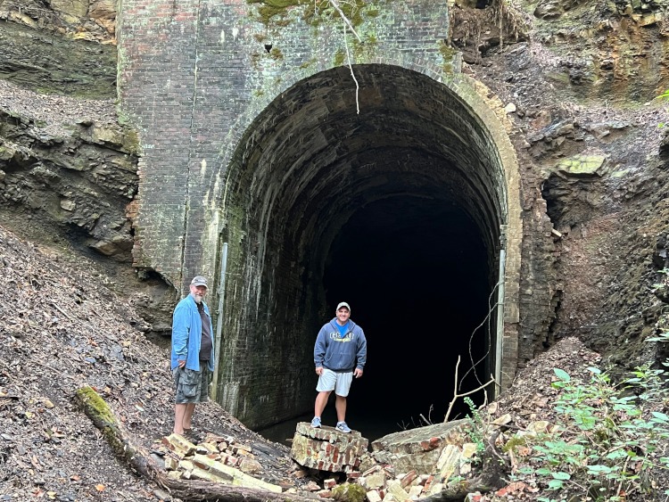 Two people standing beside an abandoned train tunnel.