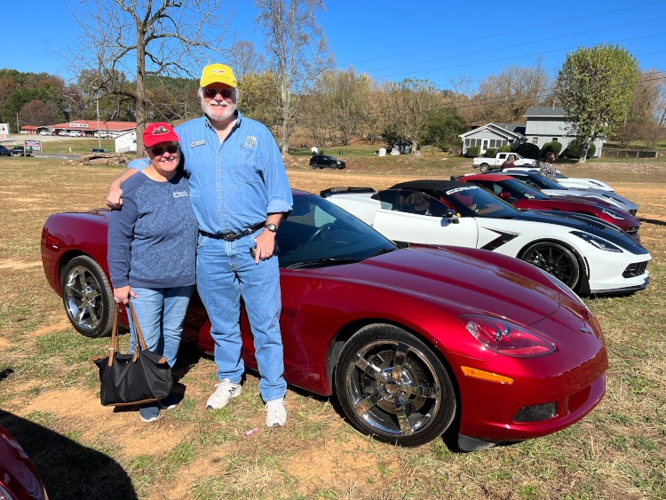 Two people standing beside a Corvette at a car show.