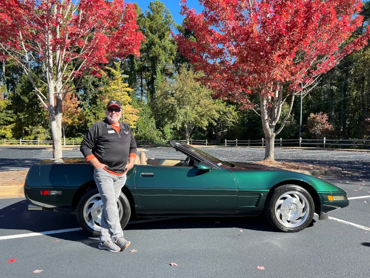 A man is standing beside a 1996 fourth-generation Corvette roadster.