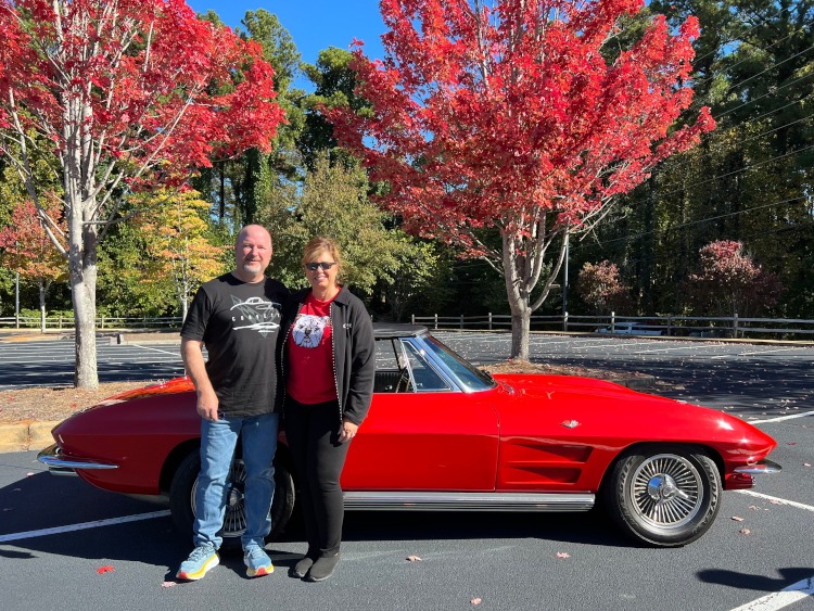 Two people standing beside a red second-genertion Corvette.