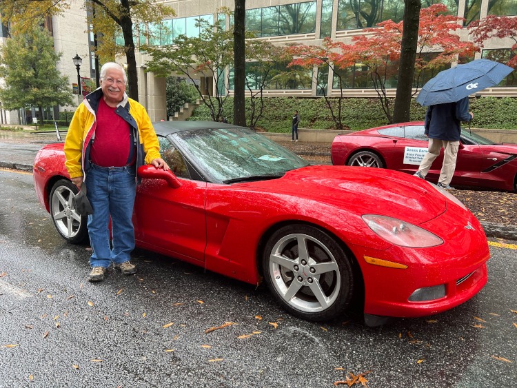 A veteran is standing beside a red C6 convertible Corvette.