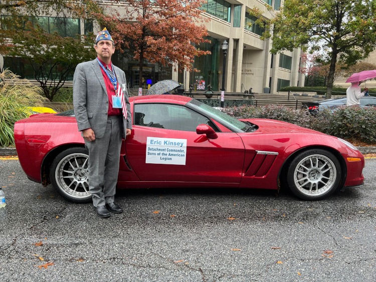 A veteran is standing beside a red sixth-generation Corvette coupe.