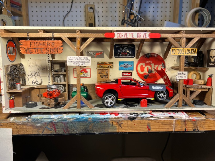 A red Corvette coupe in a scaled garage setting diarama.