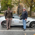 Two people standing beside a silver seventh-generation Corvette