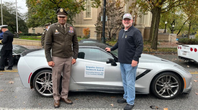 Two people standing beside a silver seventh-generation Corvette