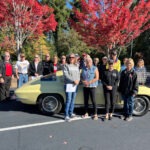 A group of Corvette enthusiasts standing around a second-generation Corvette.