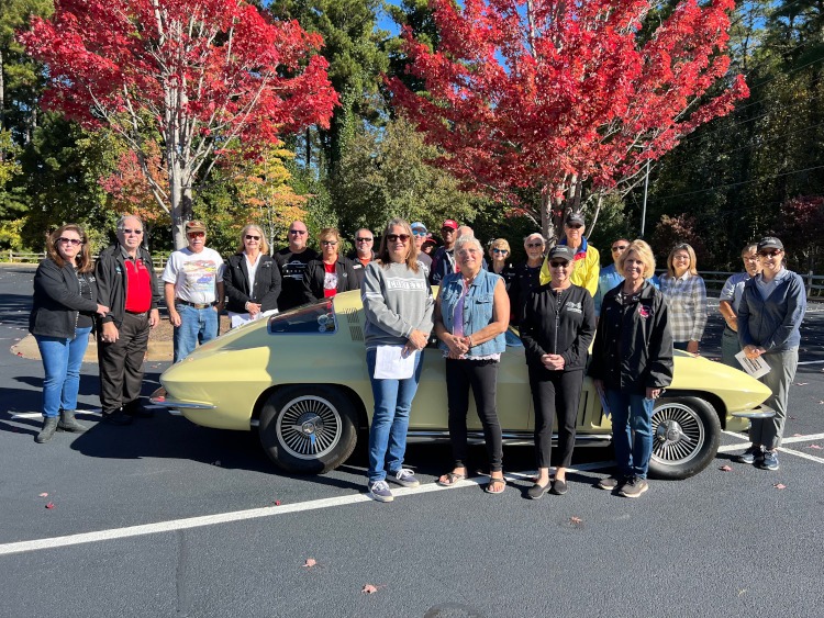 A group of Corvette enthusiasts standing around a second-generation Corvette.