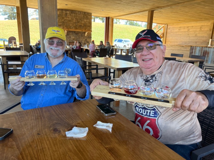 Two men holding a rack of cider glasses.