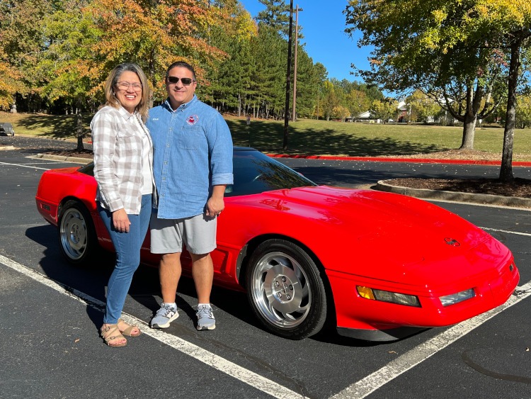Two people standing beside a four-generation Corvette