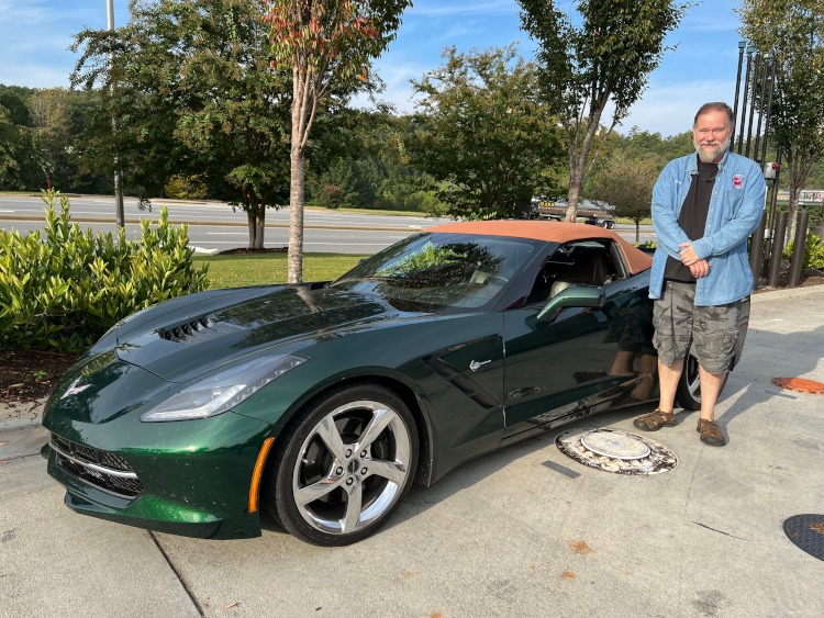 A man is standing beside a green C7 Corvette with a tan top.