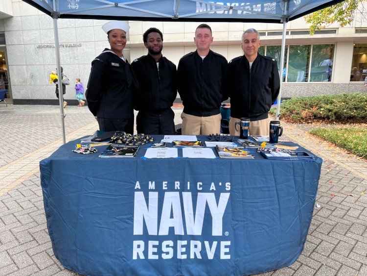 Four people standing under a Navy Reserve tent.
