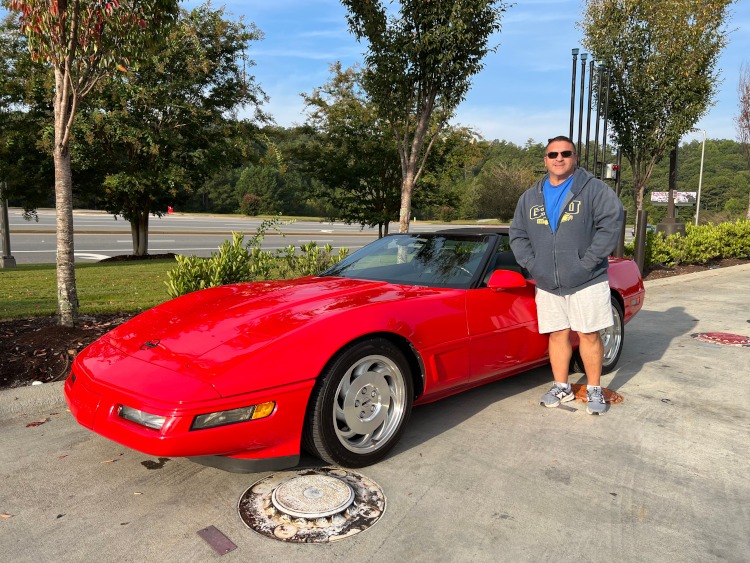 A man is standing beside a red C4 generation Corvette