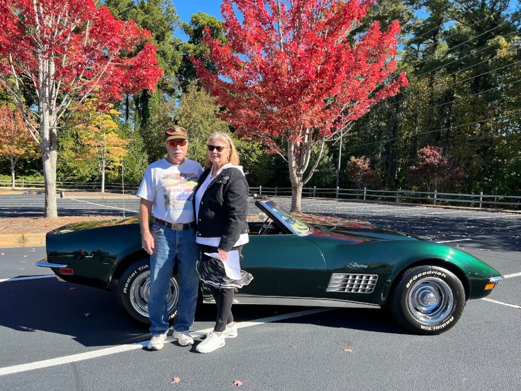 Two people are standing beside a third-generation C3 green Corvette convertible.