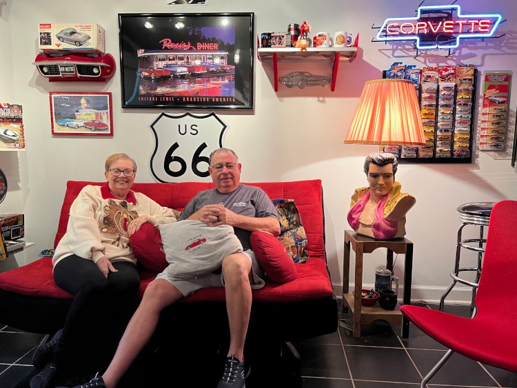Two people sitting on a couch in a Corvette man cave.