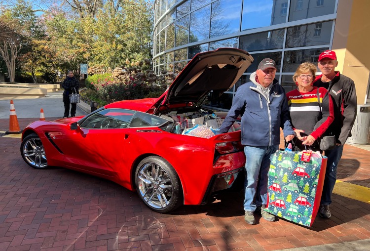 People standing beside a red Corvette filled with toys.