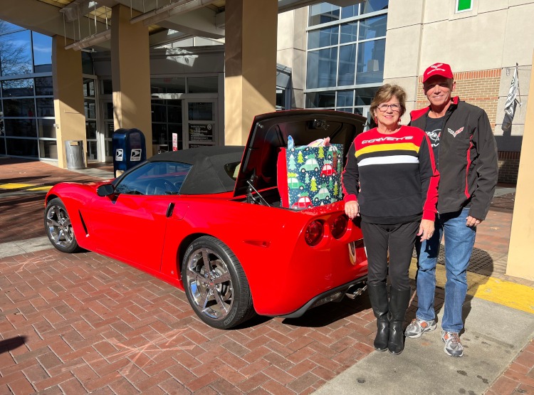 Two people standing beside a C6 red convertible Corvette with toys in the trunk.