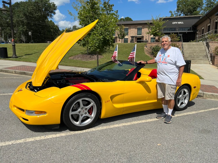 A man is standing beside a yellow C5 Corvette convertible.