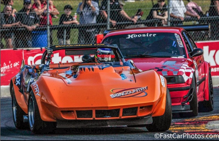 An orange C3 race car battles on a road course.