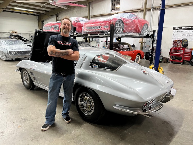 A man stands beside a silver 1963 second-generation Corvette split window coupe.