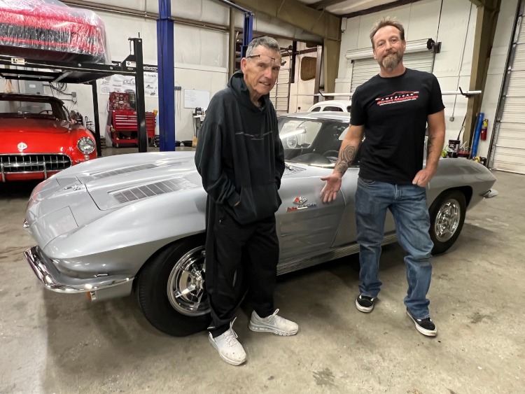 Two men are standing beside a second-generation Corvette coupe.