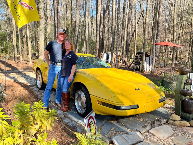 Two people standing beside a yellow C4 Corvette