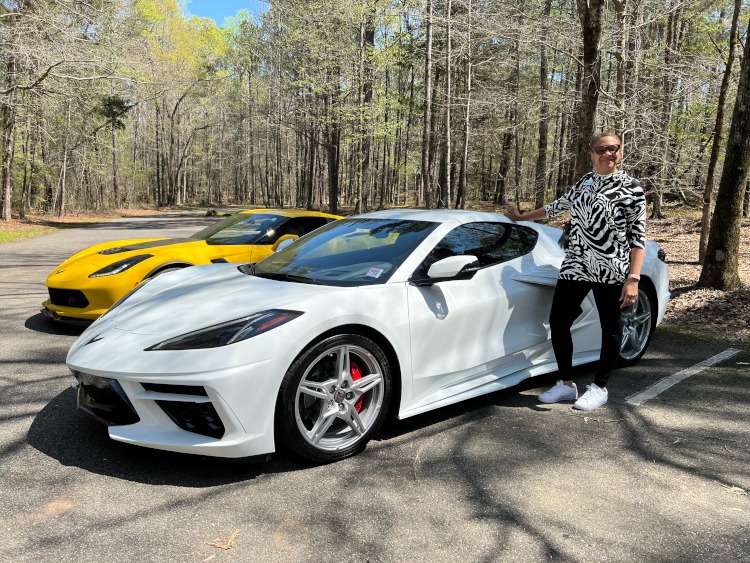 A woman standing beside an Arctic White C8 Corvette.