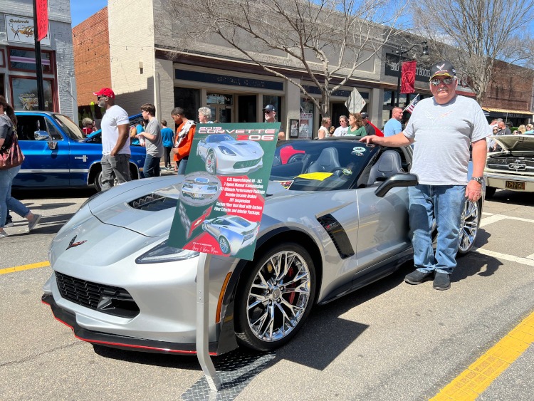 A man standing beside a gray 2015 silver Corvette coupe