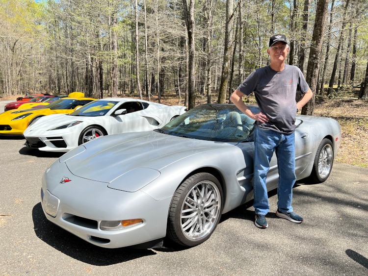 A man standing beside a silver Corvette convertible.