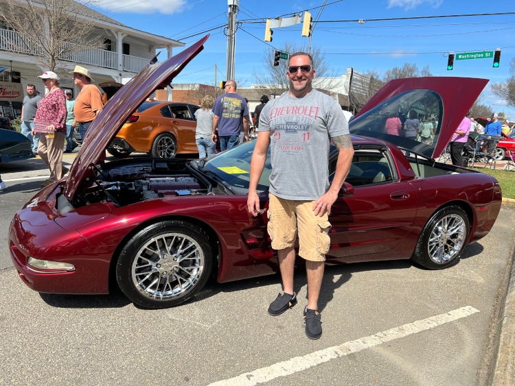 A man is standing beside a 50th anniversary Corvette coupe.