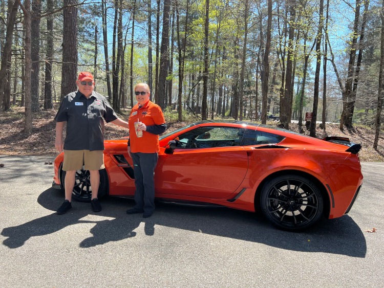 Two people standing beside their orange Corvette.
