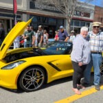 Two people standing beside a yellow Corvette convertible.