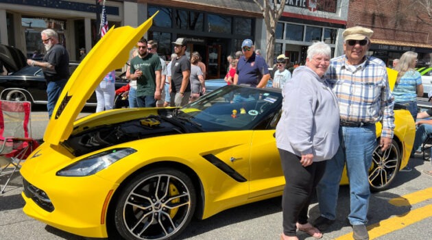 Two people standing beside a yellow Corvette convertible.