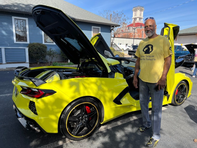 A man is standing beside a 2022 yellow Corvette coupe.