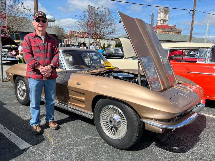A man standing beside a brown 1963 split-window Corvette coupe.