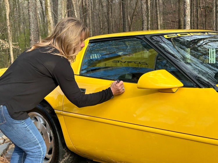 A woman is signing ther passenger door of a Corvette.