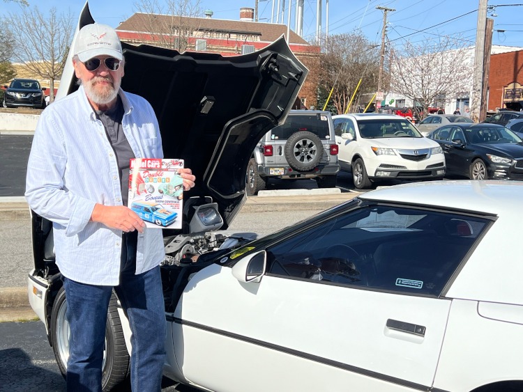 A man is standing beside a white fourth-generation Corvette.