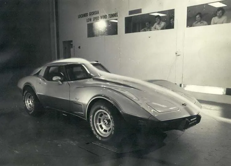 A vintage black and white photo shows a two-tone 1978 Chevrolet Corvette Pace Car in a wind tunnel. "LOCKHEED GEORGIA LOW SPEED WIND TUNNEL" is visible on the wall. Observers are seen through windows in the background, and the car's body shows airflow indicators.