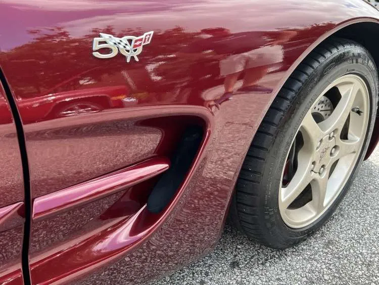 The passenger side front fender of a Anniversary Red 2003 Corvette C5, highlighting the 50th Anniversary badge, side vent, and front wheel.