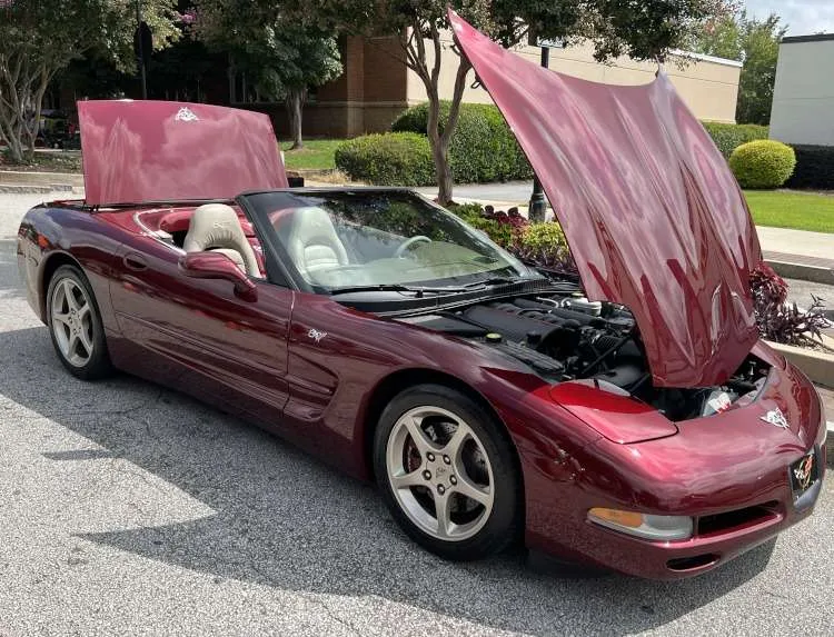 Side view of an Anniversary Red 2003 Corvette C5 convertible with its hood and trunk open, revealing the engine bay and interior.