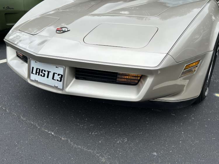 Front bumper and hood view of a 1982 Corvette Collector Edition in Silver-Beige, featuring a "LAST C3" license plate and the crossed-flags nose emblem.